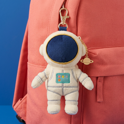 Ivory astronaut charm with teal chest panel on coral backpack
